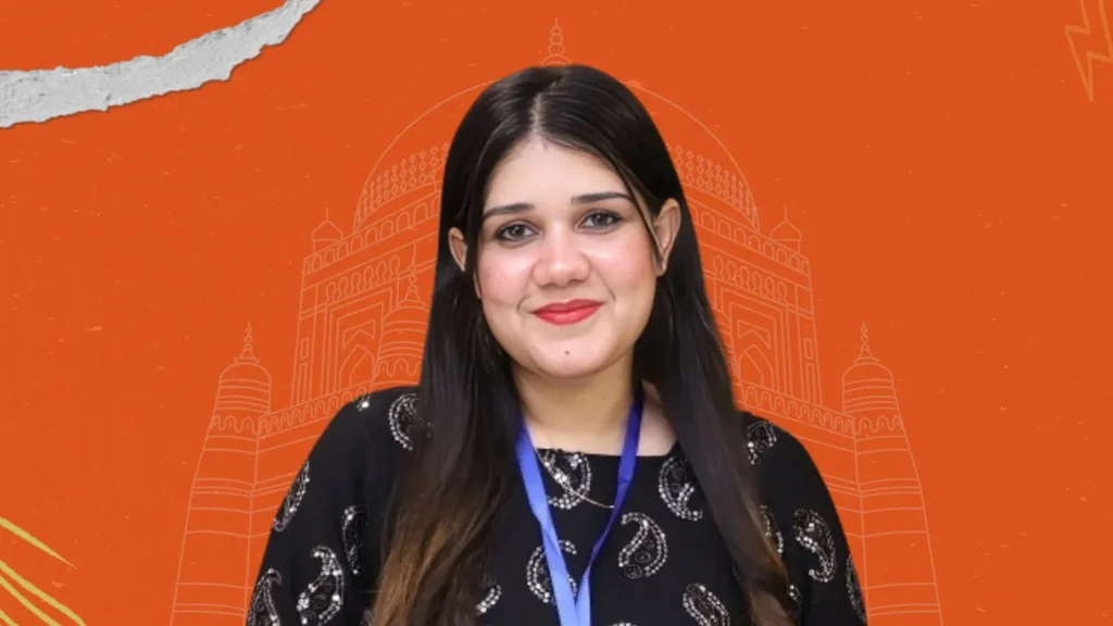 Mujhe with a confident smile in front of Multan heritage backdrop on orange theme