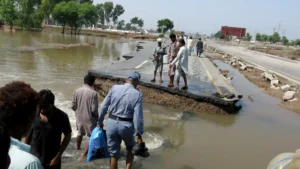 Residents crossing damaged Muzaffargarh road in Multan after authorities breached the road to ease flood pressure and protect communities.