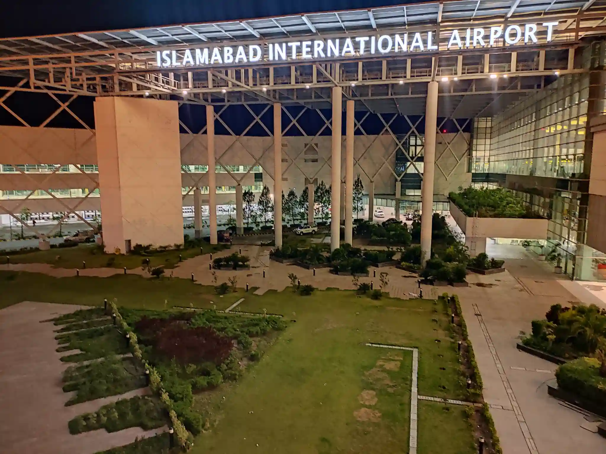 Islamabad International Airport main entrance at night with modern architecture and green landscape.