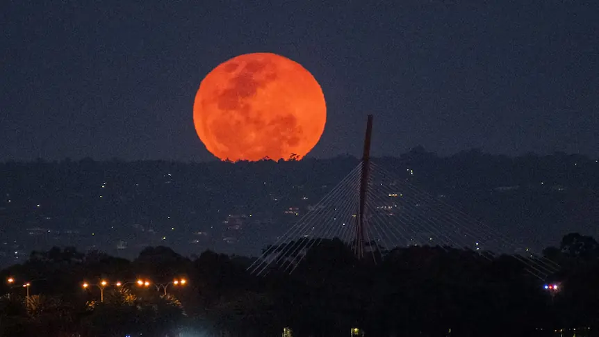 The first Supermoon of 2025 glowing bright orange in the night sky over city landscape in Pakistan