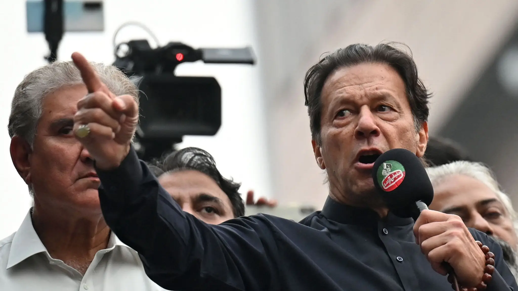 Imran Khan addressing supporters with a microphone, pointing forward, during a political gathering