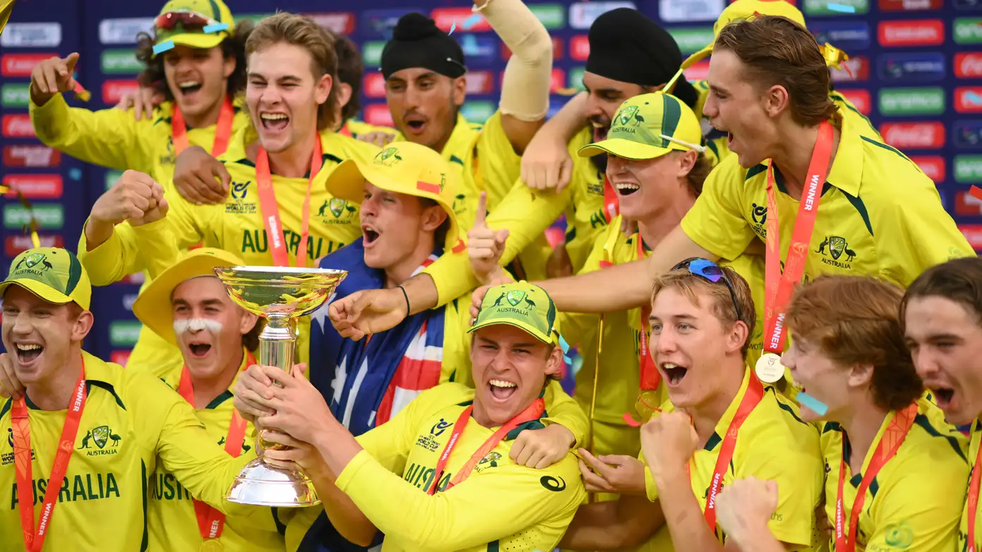 A group of young cricketers celebrating with a trophy after winning an international youth cricket tournament.