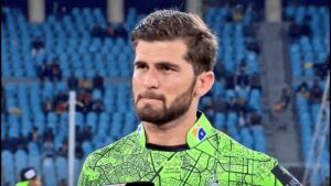 Shaheen Shah Afridi sitting on the field in Pakistan team uniform, reflecting during a match amid PCB hotel security concerns.