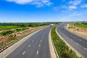 "Wide view of a modern six-lane motorway surrounded by green fields, with clear skies and well-maintained road infrastructure.