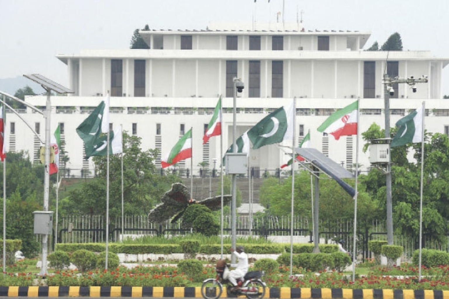 A man riding a motorcycle past the President House in Islamabad, decorated with Pakistani and Iranian flags ahead of the US-Iran peace negotiations.