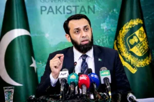 "Press conference by Pakistani Information Minister Attaullah Tarar, speaking about national issues with microphones and flags in the background."