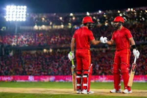 Two cricketers in red uniforms celebrating with a fist bump during the PSL 11 final, illuminated by bright stadium lights with a cheering crowd in the background."