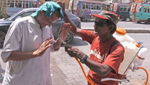 A volunteer spraying water on a citizen to provide relief during a heatwave, related to the Karachi weather update.