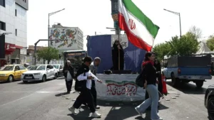 People walking near an Iranian flag in Tehran during discussions surrounding the Iran Peace DealPeople walking near an Iranian flag in Tehran during discussions surrounding the Iran Peace Deal