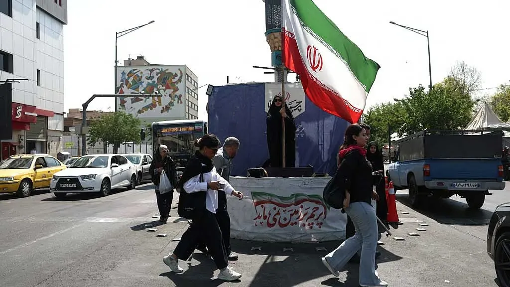 People walking near an Iranian flag in Tehran during discussions surrounding the Iran Peace DealPeople walking near an Iranian flag in Tehran during discussions surrounding the Iran Peace Deal