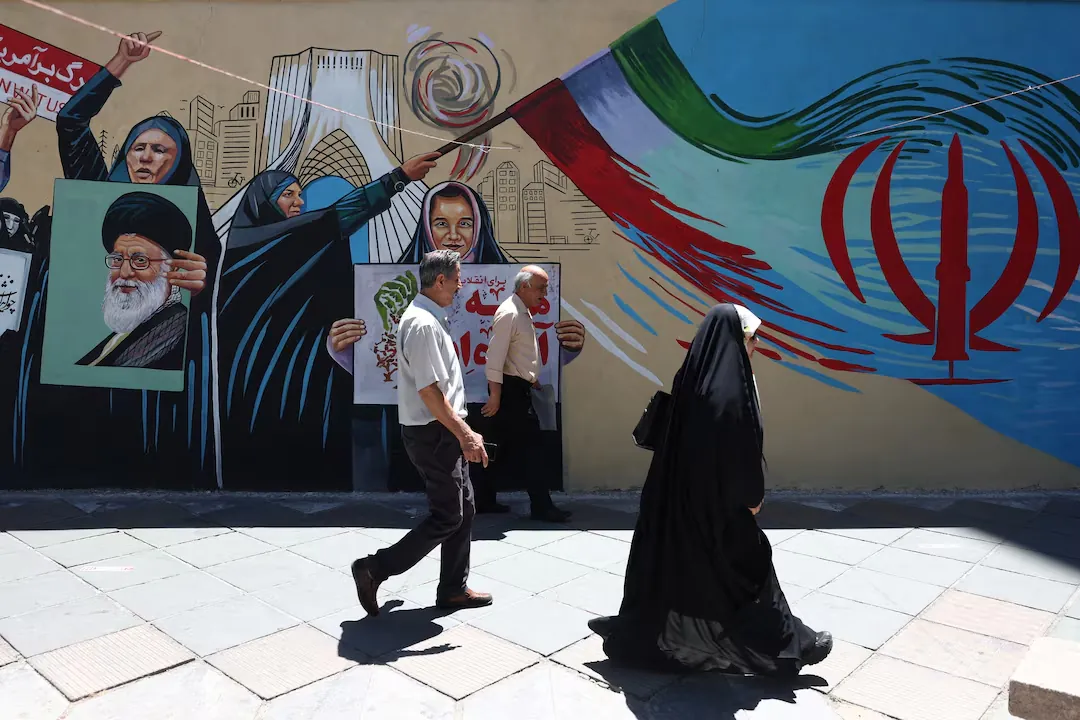 People walk past a mural featuring Iranian national symbols and political imagery in Tehran during discussions over the Iran US Deal.