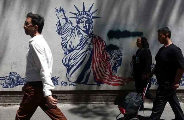 Pedestrians walk past a mural in Tehran as discussions over the Iran War Deal continue amid ongoing regional tensions.