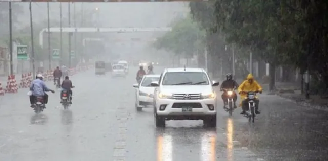 Vehicles and motorcyclists traveling on a rain-soaked road during Karachi Rain as light showers improve weather conditions
