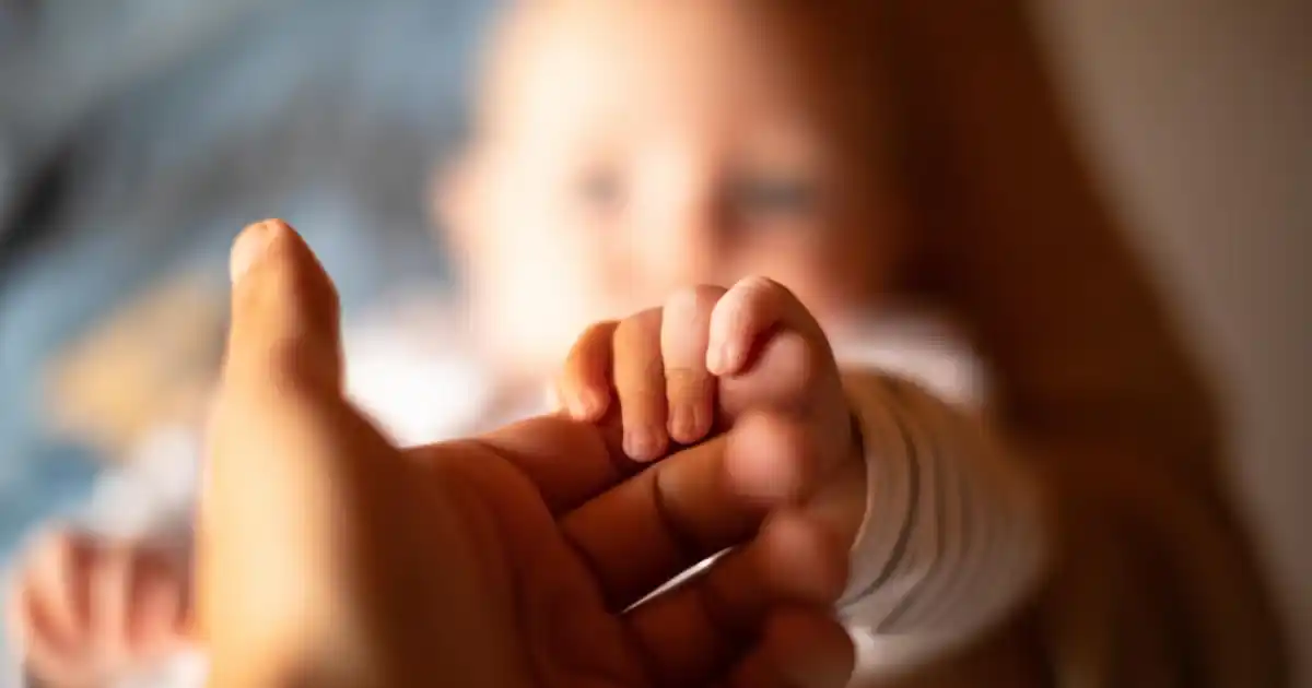 A newborn baby holds an adult's finger, representing the France Surrogacy ruling on legal recognition of children born through overseas surrogacy.
