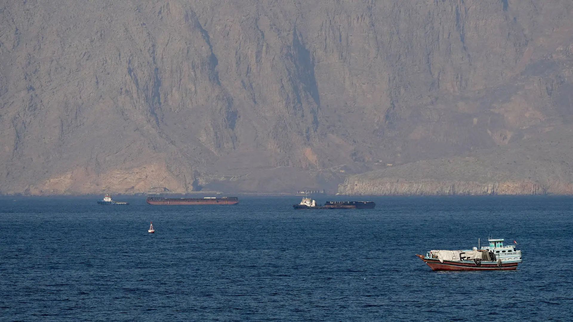 Commercial cargo ships and boats navigating the waterway near Musandam, Oman, amid geopolitical disputes over proposed Hormuz Strait Fees.