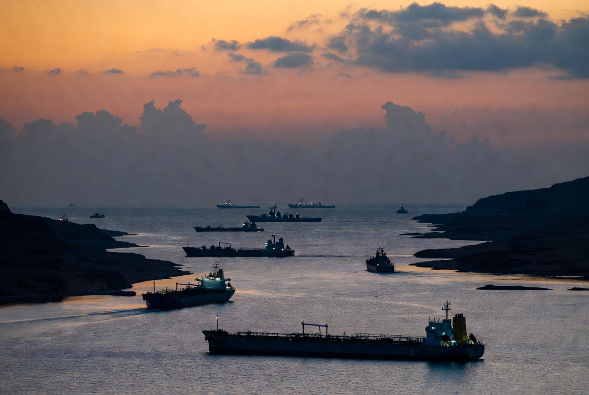 Oil tankers and naval vessels in the Strait of Hormuz at dusk amid Iran halt strikes and US bombing pause