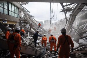Rescue workers in orange uniforms searching through rubble of a damaged shopping mall after Japan quake toll rises