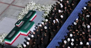 Mourners gather during the Khamenei funeral prayer in Tehran as family members stand beside the coffins.