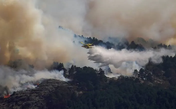 Firefighting aircraft drop water over a forest fire during Spain Wildfires as extreme heat fuels blazes across Southern Europe.