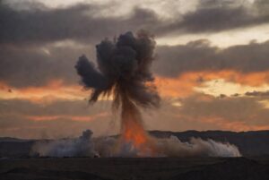 Thick smoke rising from a large explosion in the desert at dusk during US strikes Iran