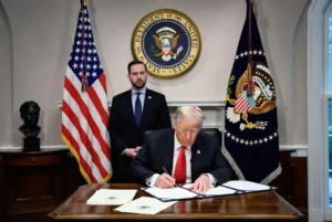 President Donald Trump signing birthright citizenship executive orders at the White House Oval Office desk with official flags and documents