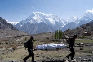 Rescue personnel carrying covered stretcher with climber body from Broad Peak tragedy against snow-capped mountains near Skardu