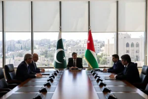 Deputy Prime Minister Ishaq Dar seated at conference table during Dar Jordan Visit with Pakistan and Jordan flags in background at Amman ministerial meeting