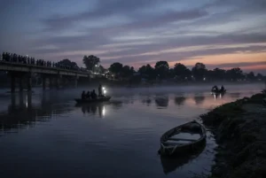 Rescue personnel searching the Ganges river after Bihar boat tragedy with villagers watching from the bridge at dusk
