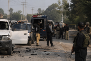 Security personnel investigate a roadside attack scene in DI Khan, with police vehicles and officers conducting operations following the killing of FBR officials and a police constable.