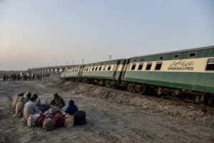 Derailed coaches of Rehman Baba Express near Sher Shah Bridge during Multan train derailment with passengers and luggage sitting on the ground