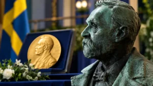 Alfred Nobel bronze bust displayed beside a Nobel medal at a formal Nobel Peace Prize setting